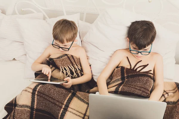Dva chlapci hrají na notebook a tablet se psem v posteli — Stock fotografie