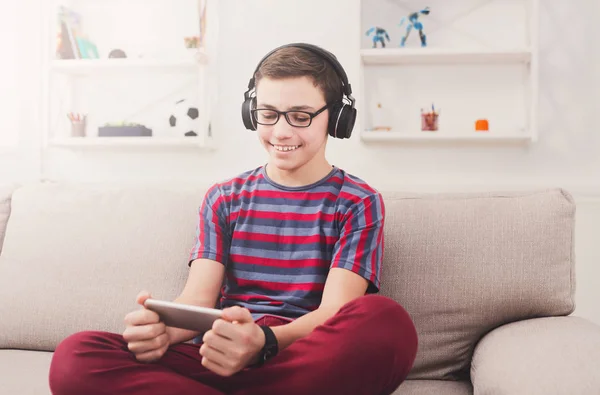 微笑着十几岁的男孩玩手机游戏在家里 — 图库照片