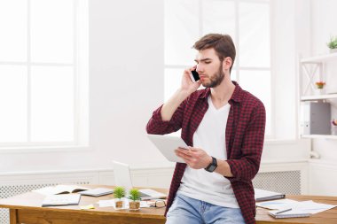 Dijital taplet kullanarak ve cep telefonu Office konuşurken dalgın genç işadamı