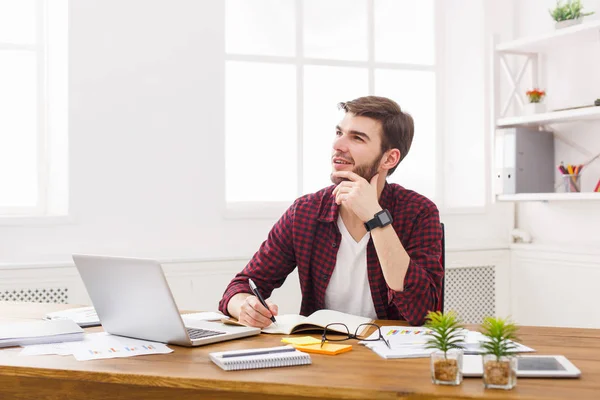 Pensivo jovem empresário toma notas no escritório branco moderno — Fotografia de Stock