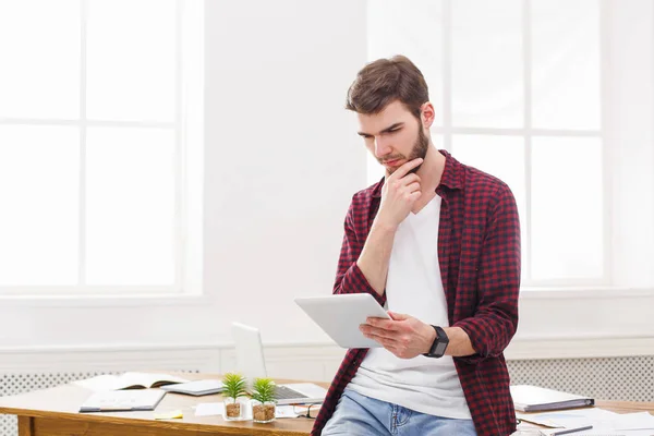 Jovem empresário pensativo usando taplet digital no escritório — Fotografia de Stock