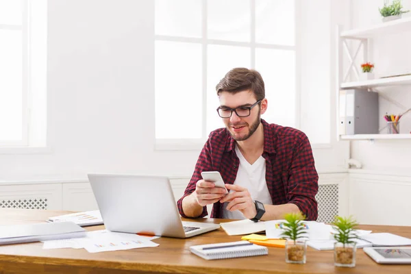 Ung glad affärsman i office med mobiltelefon av den bärbara datorn — Stockfoto