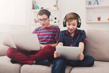 Gadget'lar ve evde kanepede kulaklık ile iki genç erkek