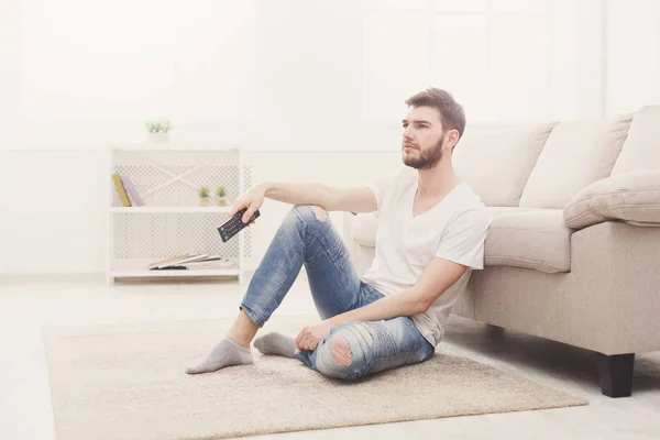 Ung man tittar på tv med fjärrkontrollen i vardagsrum — Stockfoto