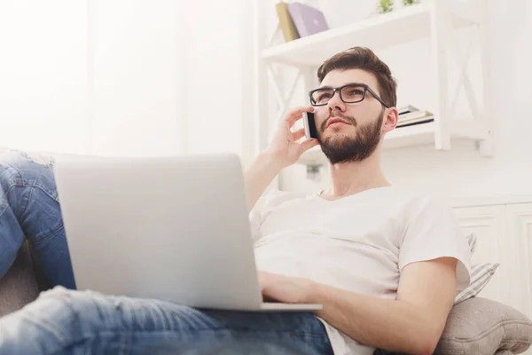 Ernstige jonge man thuis met laptop en mobiel — Stockfoto