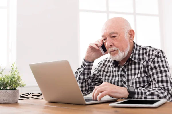 ノート パソコンと携帯電話で話している年配の男性 — ストック写真