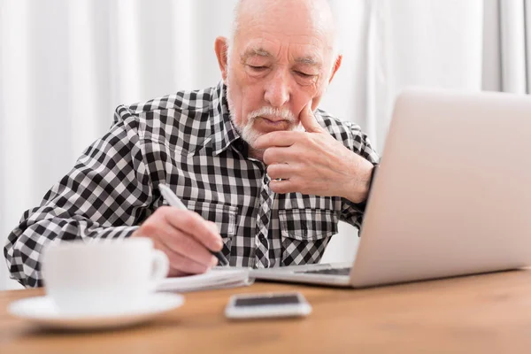 Reifer Mann benutzt Laptop und schreibt in Notizblock — Stockfoto