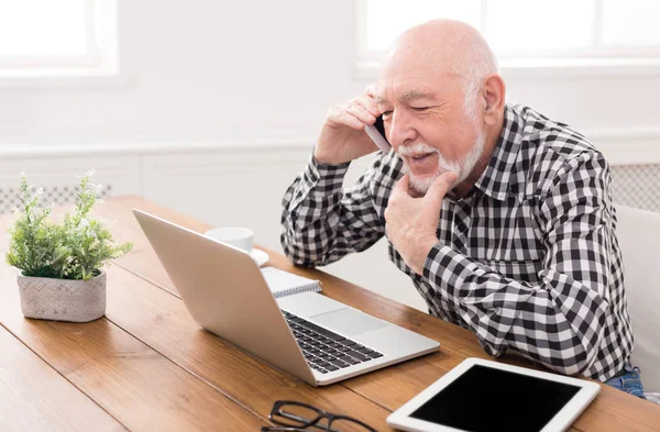 Старший чоловік розмовляє по телефону з ноутбуком — стокове фото