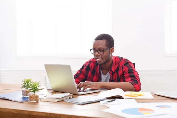 Счастливый черный бизнесмен в случайном офисе, работа с ноутбуком — стоковое фото
