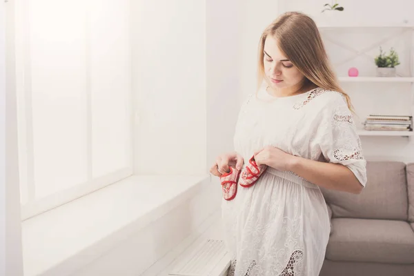 Pregnant woman holding tiny shoes near belly