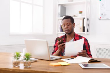 Genç siyah işadamı belgeleri, mesaj mobil modern beyaz ofis okumak