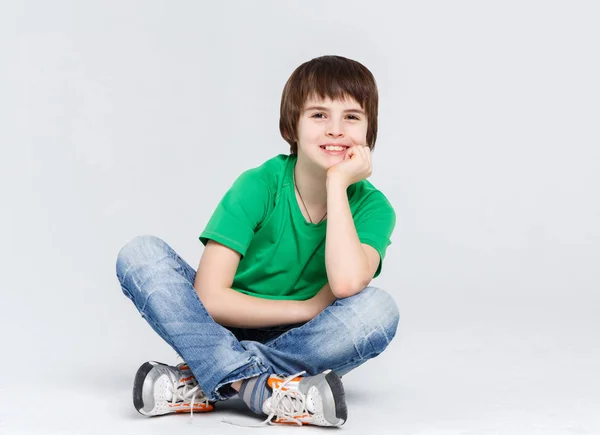 Retrato de un chico lindo sentado en el suelo sobre fondo blanco — Foto de Stock