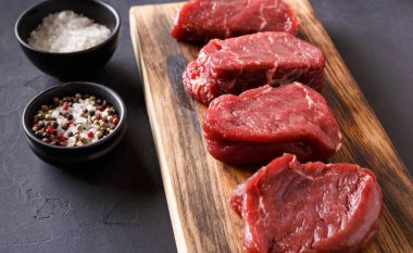 Ham sığır fileto biftek ahşap tahta at siyah arka plan üzerinde baharatlar ile