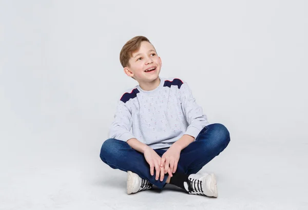 Retrato de un chico lindo sentado en el suelo sobre fondo blanco — Foto de Stock