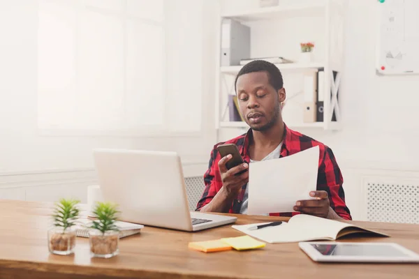 Fiatal fekete üzletember olvassa el a dokumentumok és a modern fehér office mobile textil — Stock Fotó