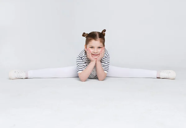 Little cute girl sitting in the splits on white studio background — Stock Photo, Image