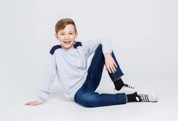 Retrato de un chico lindo sentado en el suelo sobre fondo blanco — Foto de Stock