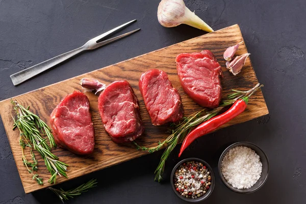 Filet mignon steaks and spices on wood at black background — Stock Photo, Image