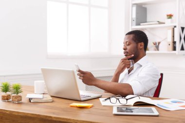 Dizüstü bilgisayarda çalışırken telefonu düşünceli Afrikalı-Amerikalı işadamı manifatura