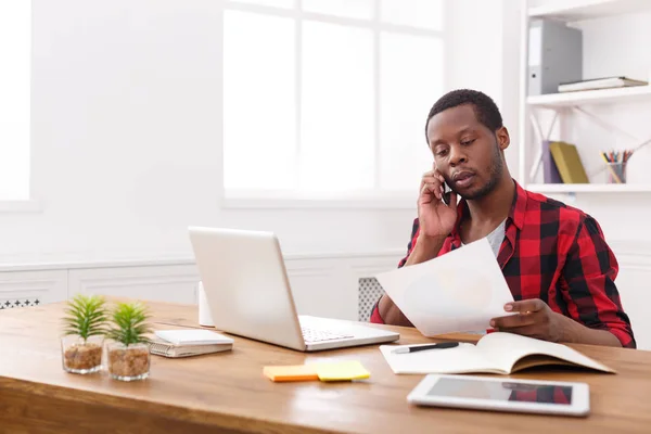 Νέοι μαύρο επιχειρηματίας ανάγνωσης εγγράφων και να μιλήσουμε στο κινητό σε μοντέρνο λευκό γραφείο — Φωτογραφία Αρχείου
