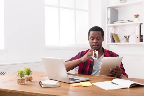 Hombre de negocios negro en la oficina informal, la lectura de noticias en la tableta, beber café —  Fotos de Stock