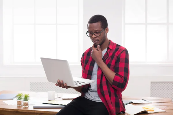 Doordachte zwarte zakenman in casual kantoor, werken met een laptop — Stockfoto