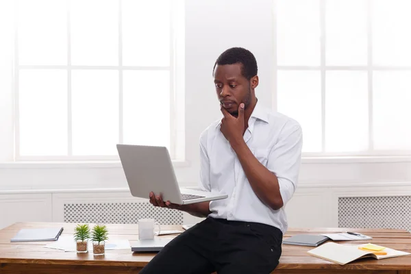 Homem de negócios preto pensativo no escritório casual, trabalho com laptop — Fotografia de Stock