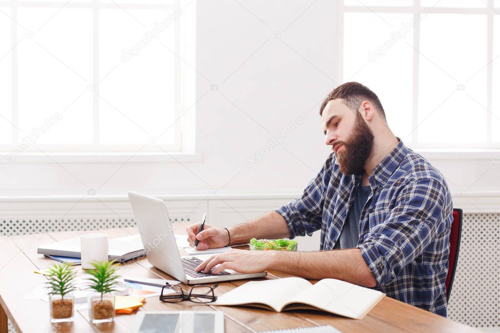 Busy male programmer has business lunch in modern office interior