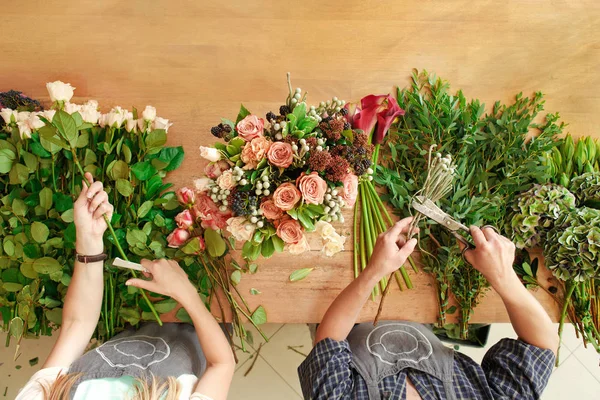 Fiorista e assistente nella consegna negozio di fiori fanno bouquet rosa, vista tavolo dall'alto — Foto Stock