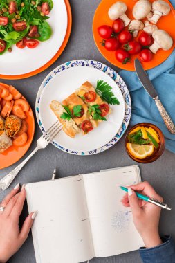 Gri arka plan üzerinde üstten görünüm sağlıklı yemek yerken notlar alarak kadın.