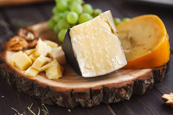 Käseplatte, Parmesan auf Naturholzscheibe mit Trauben und Nüssen — Stockfoto