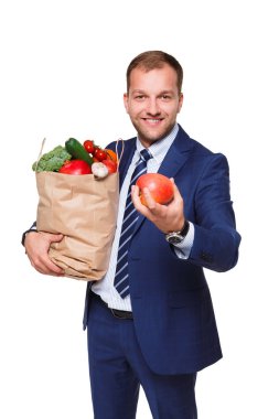Alışveriş çantası beyaz arka plan üzerinde izole sebze dolu tutarak gülümseyen iş adamı.