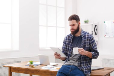 Delikanlı ile modern işyeri iç dijital tablet kullanarak kahve masasında rahat oturmak.