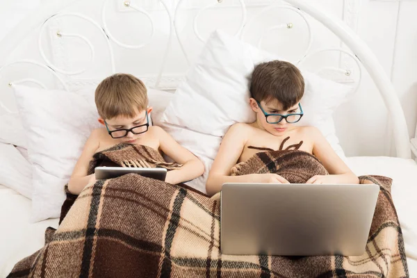 Два мальчика играют в ноутбук и планшет с собакой в постели — стоковое фото