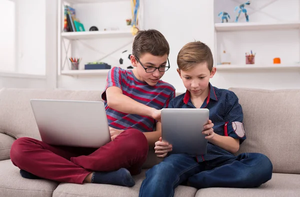 İki genç çocuklar evde kanepede gadget'lar ile — Stok fotoğraf