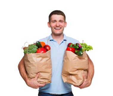 Beyaz arka plan üzerinde izole sebze dolu poşetler tutan gülümseyen genç adam.