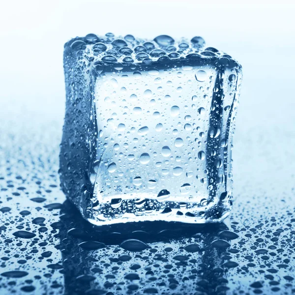 Cubo de hielo transparente en vidrio azul con gota de agua — Foto de Stock