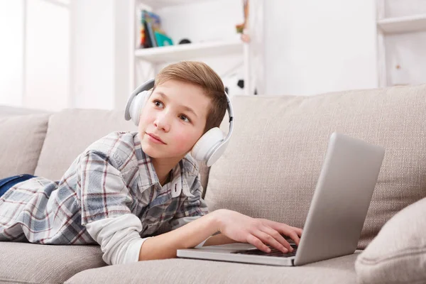 Мальчик-подросток в наушниках с ноутбуком дома — стоковое фото