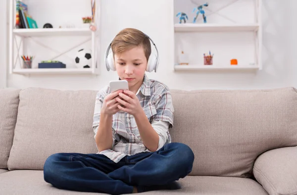 Tonårspojke med tandställning i hörlurar spelar spel på smartphone — Stockfoto