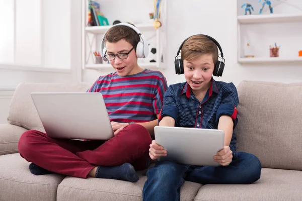 Dos adolescentes con gadgets y auriculares en el sofá en casa — Foto de Stock