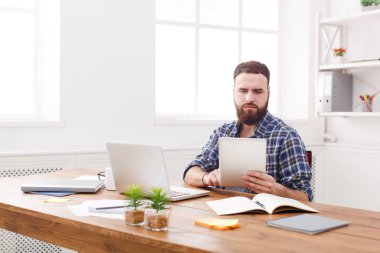 Genç adam masada dizüstü bilgisayar ile tablet kullanarak konsantre