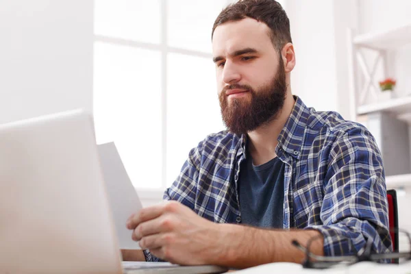 Close up of a serious man office worker is reading report, while is sitting at the table with open net-book. — Stock Photo, Image