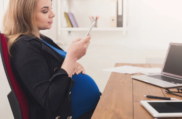 Молодая беременная женщина использует смартфон в офисе — стоковое фото