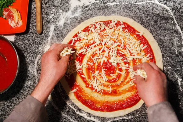 Reibekäse zur Pizza von oben hinzufügen — Stockfoto