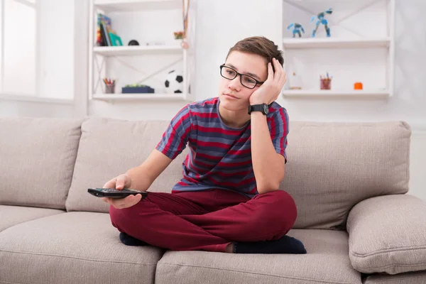 Boy watching tv and looking bored on couch at home