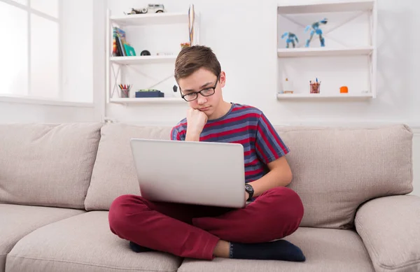 Грустный подросток использует ноутбук на диване дома — стоковое фото