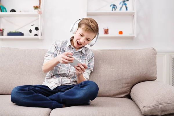 Мальчик-подросток с брекетами в наушниках играет в игры на смартфоне — стоковое фото