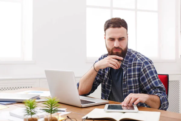 Närbild porträtt av en fundersam ung affärsman sitter och använder tablet PC i office — Stockfoto