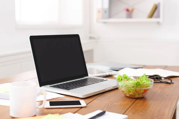 Side view of office desk with salad, laptop, smartphone and other items