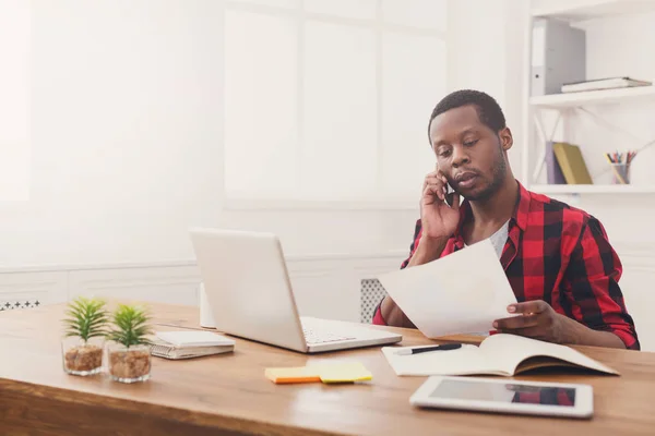 Jonge zwarte zakenman Lees documenten en praten op mobiele in moderne witte kantoor — Stockfoto